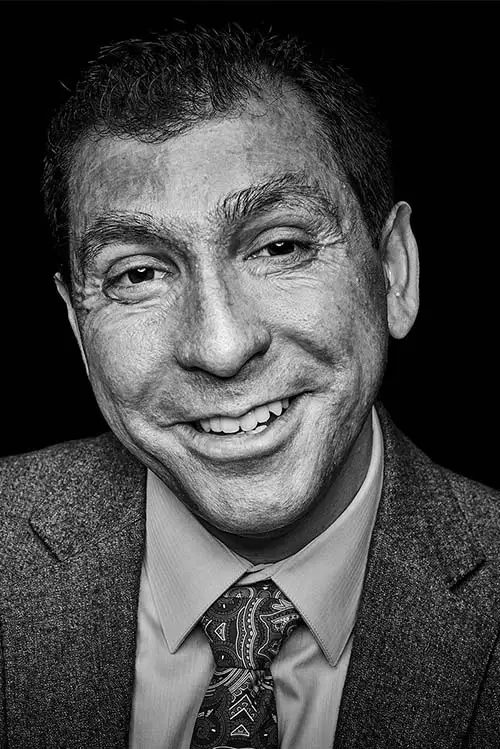 Tulio K. Cardozo, smiling, in a tweed jacket and patterned tie